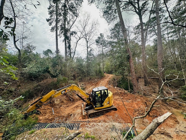CAT excavator setting culvert pipe along a woodland road